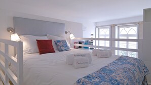 A bedroom with a bed, pillows, a bedside table, a lamp, and a window. - FLH Porto Cozy Studio (Oporto)