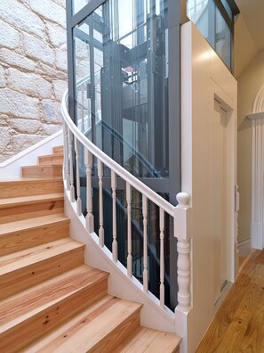 A wooden staircase with white balusters leading to a glass elevator.