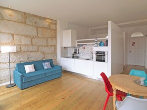 Un espace de vie compact comprenant un coin cuisine, un canapé bleu, une table à manger avec des chaises rouges et un mur décoratif en pierre.
