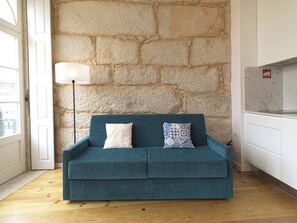 A teal sofa with patterned cushions against a stone wall, a lamp, and a white cabinet.