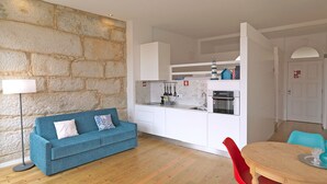 A compact living space with a kitchenette, a blue sofa, a dining table with red chairs, and a stone accent wall. - FLH Porto Cozy Studio (Oporto)