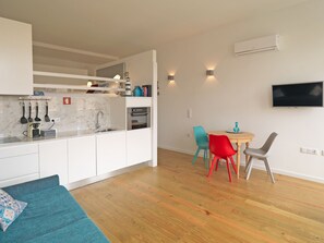 A modern kitchen with white cabinets, a built-in oven, and a marble backsplash. There is a dining area with a wooden table and colorful chairs.