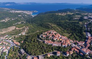 An aerial view of a coastal town with a central historic area featuring red-roofed buildings, surrounded by lush greenery and a coastline. - Beautiful home in Topid with sauna (Topid)