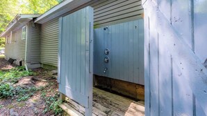 Een houten tuinhuis met een metalen deur, een klein raam en een houten terras.