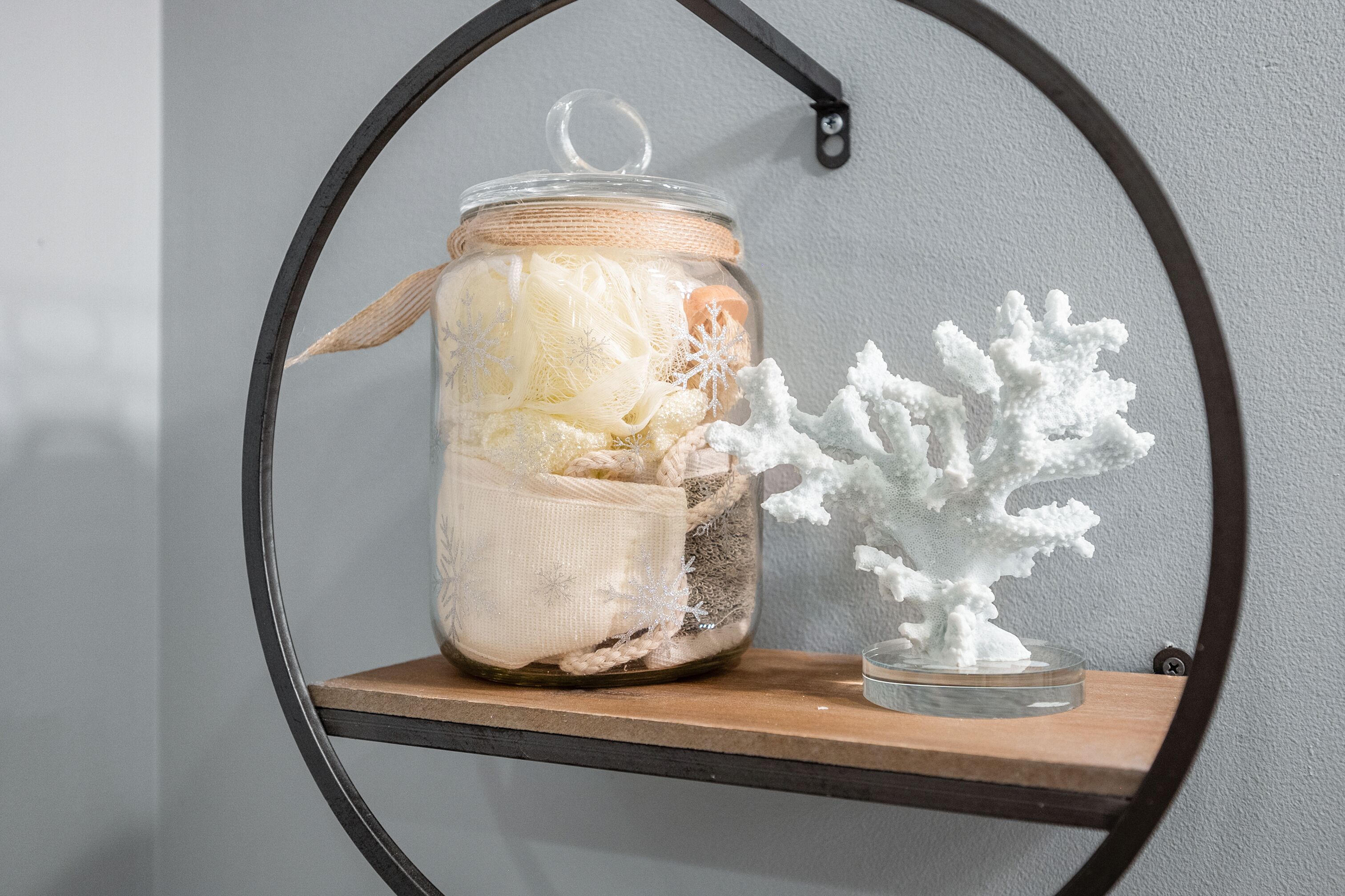 Un frasco de vidrio con tapa en un estante, que contiene varios objetos y una pequeña escultura blanca con forma de árbol junto a él.