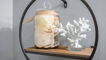 Un frasco de vidrio con tapa en un estante, que contiene varios objetos y una pequeña escultura blanca con forma de árbol junto a él.