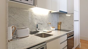 Una cocina moderna con armarios blancos, microondas integrado, fregadero, tostadora y lavavajillas.