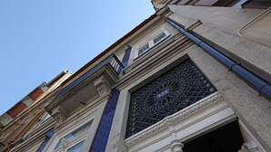 Fachada de edificio con una ventana que presenta ornamentación metálica intrincada y una columna con azulejos azules.