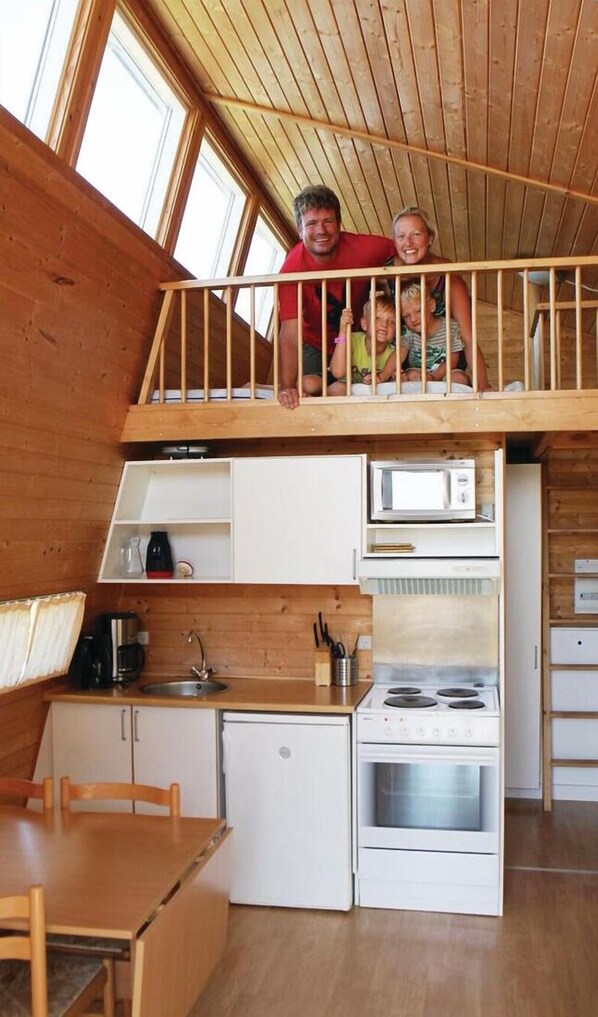 Una cocina compacta con estufa, microondas y fregadero, un refrigerador pequeño, y un comedor con mesa y sillas.