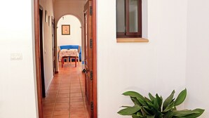 Ein Flur, der in einen Essbereich mit Tisch und Stühlen, ein kleines Fenster und einer Zimmerpflanze führt.