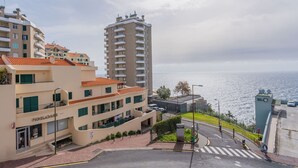 Zona residencial costera con un edificio alto, un edificio más pequeño con el letrero 'FIDELDA', y vista al mar.