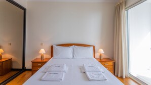 Una habitación de hotel con una cama grande, dos mesitas de noche con lámparas y un ventanal con cortinas.