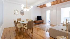Un salon moderne comprenant un coin repas, un plancher en bois, un canapé, un téléviseur et un luminaire au plafond.