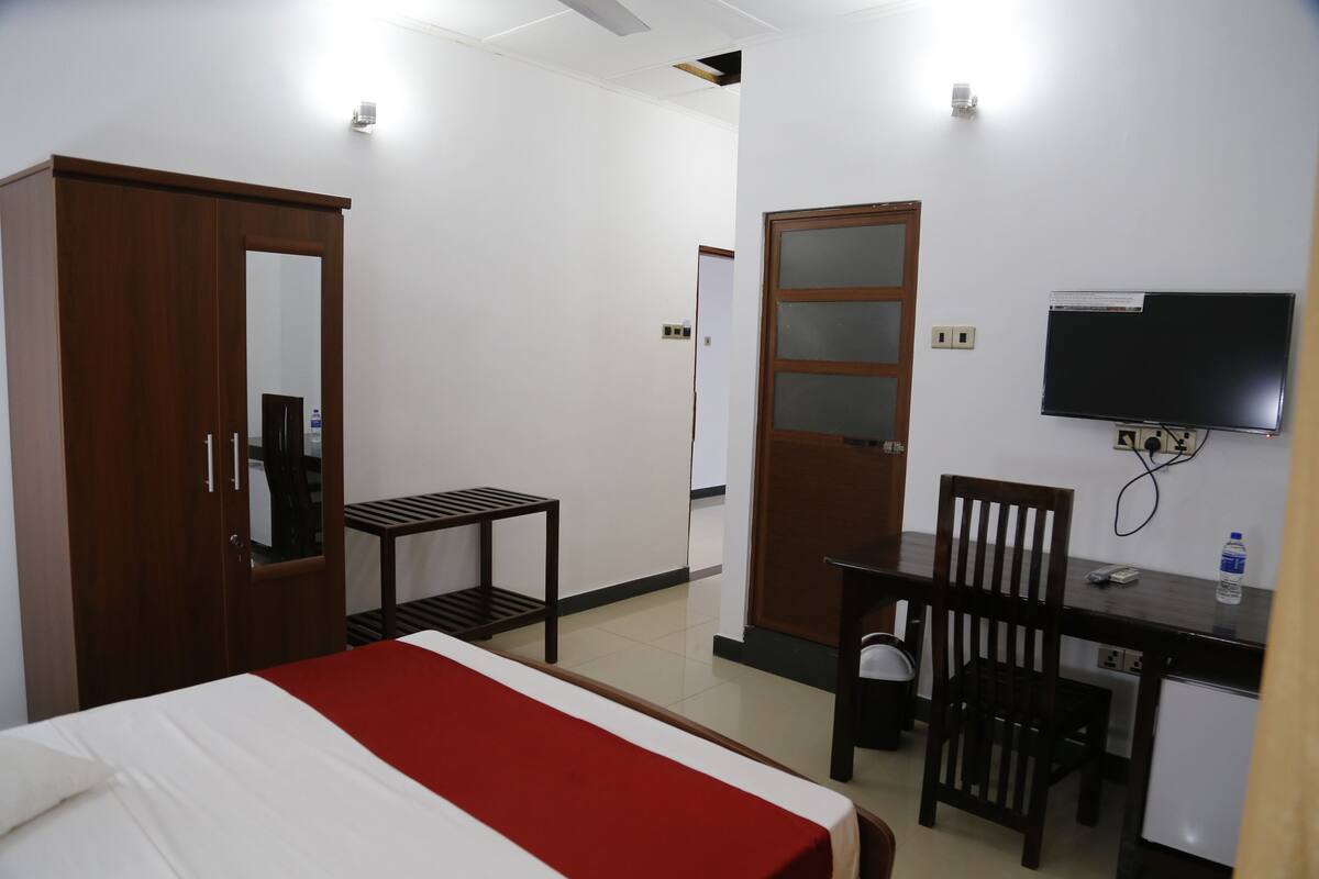 A hotel room with a bed, a desk, a chair, a wardrobe, and a TV.