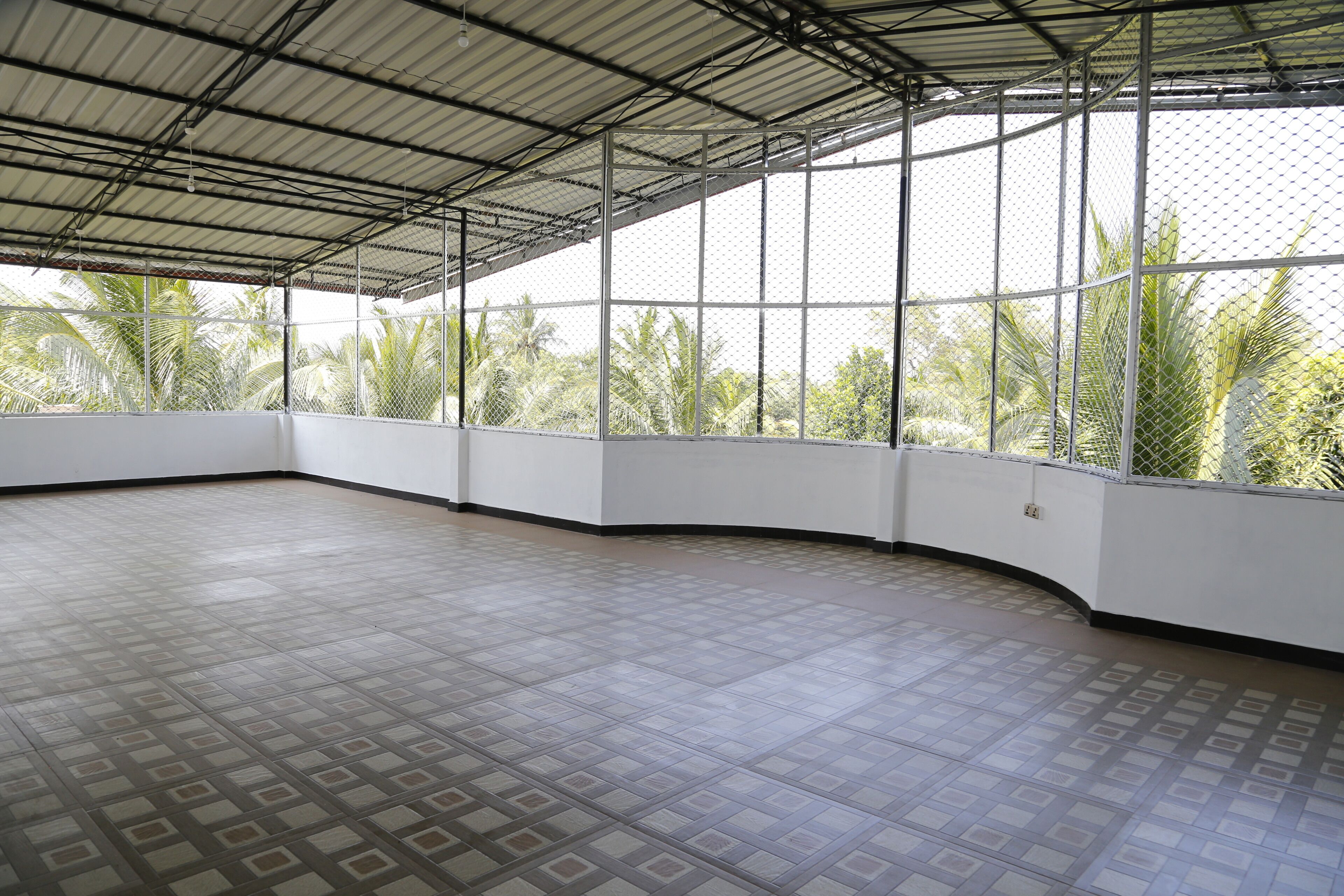 Amplia habitación con techo alto y ventanas grandes, con vistas a palmeras.