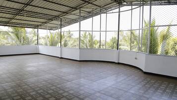Amplia habitación con techo alto y ventanas grandes, con vistas a palmeras.