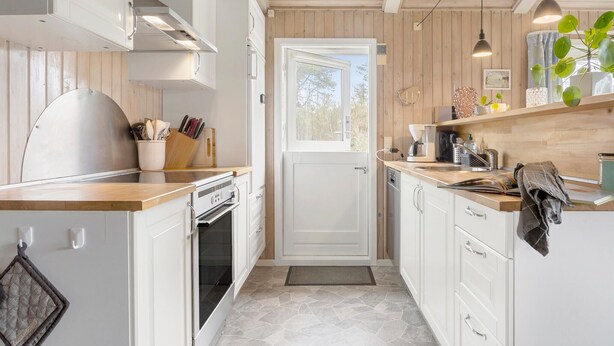 A compact kitchen with white cabinetry, a wooden countertop, a built-in oven, and a window with a view of trees.