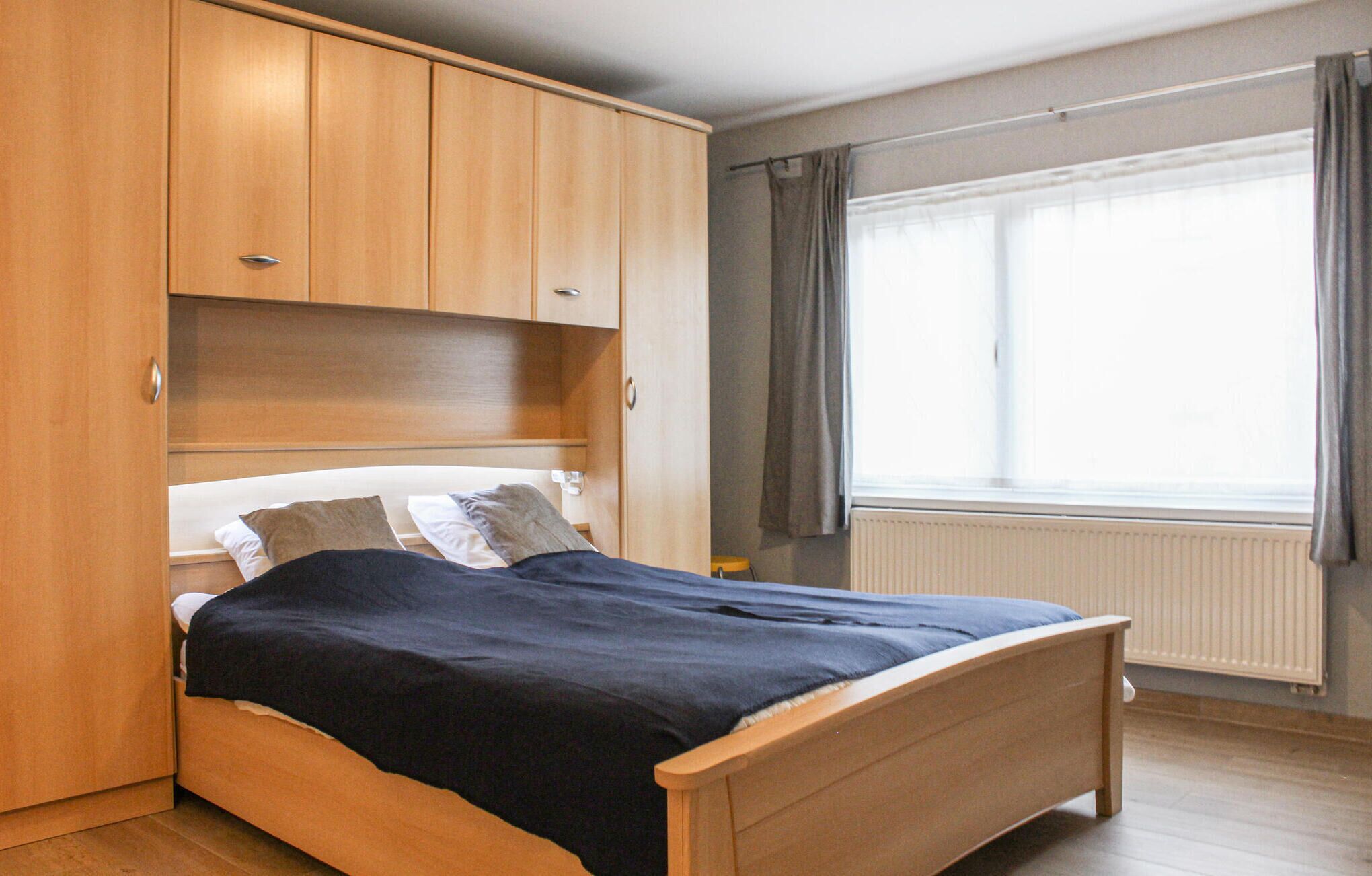 Ein Schlafzimmer mit einem hölzernen Bett, einem eingebauten Kleiderschrank und einem Fenster mit Vorhängen.