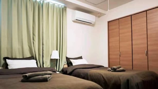 A hotel room with two beds, a wardrobe, and an air conditioning unit. - Sun Hotel (Tokyo)