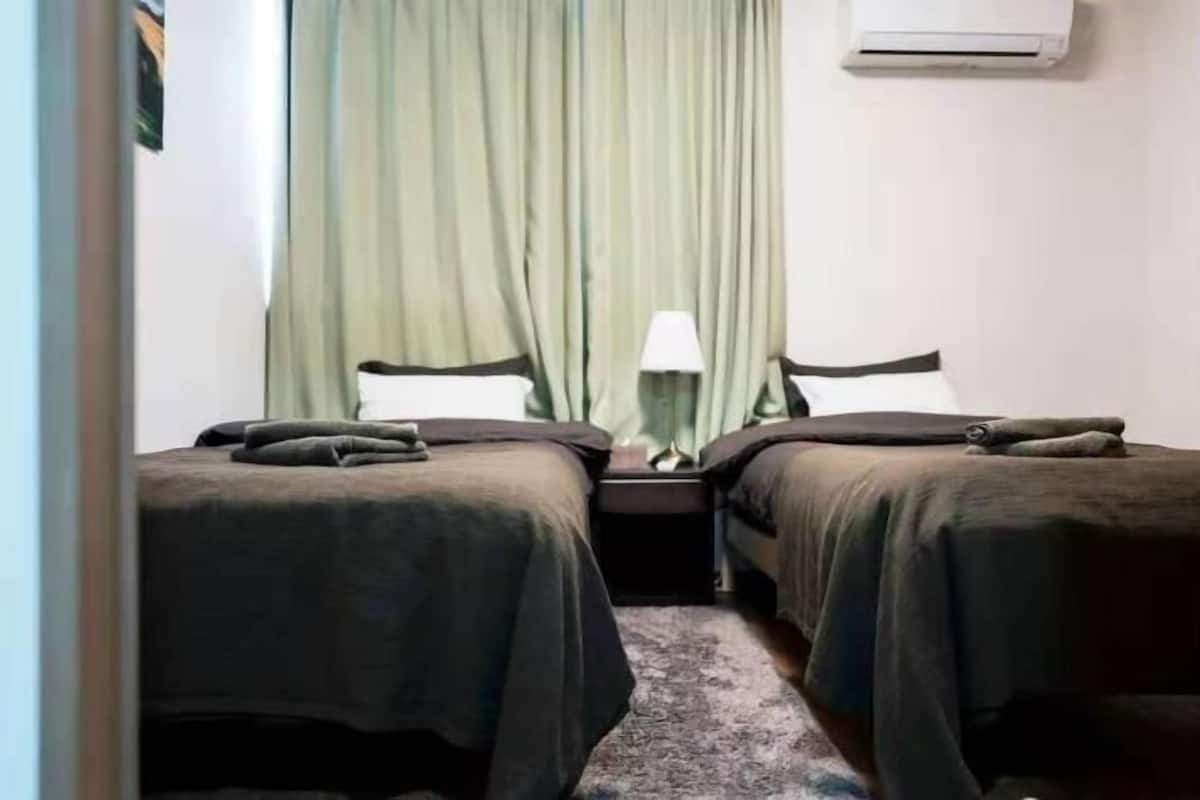 A hotel room with two beds, a nightstand, a lamp, and a window with curtains.