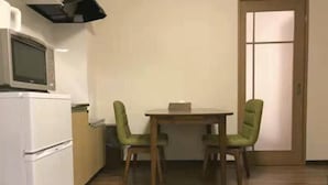 A small kitchen with a microwave, a refrigerator, and a dining table with two chairs. - Sun Hotel (Tokyo)