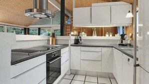 A modern kitchen with white cabinetry, a stainless steel range hood, a built-in oven, and a black countertop. - 4 bedroom beautiful home in Saltum (Saltum)