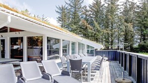 A covered outdoor seating area with metal chairs and tables, surrounded by glass doors and windows, overlooking a forested area. - 4 bedroom beautiful home in Saltum (Saltum)