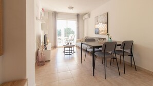 Una sala de estar moderna con un sofá, una mesa de comedor y sillas. Hay un ventanal con cortinas, una chimenea y un cuadro en la pared.