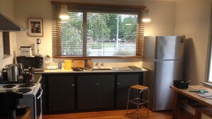 Cocina compacta con estufa, microondas, lavabo y refrigerador. Hay una ventana con persianas, un taburete pequeño y una alfombra en el suelo.