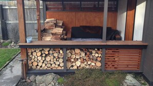 Un área de estar moderna al aire libre con un banco de madera, una pila de leña y una barandilla de metal.