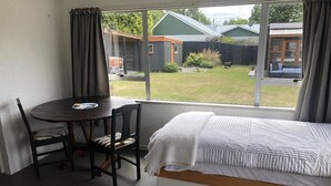 Un dormitorio con una cama, una mesita con sillas y vistas al jardín.