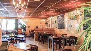 Een restaurantinterieur met houten tafels en stoelen, hangende lampen en een menukaart op een schoolbord aan de muur.