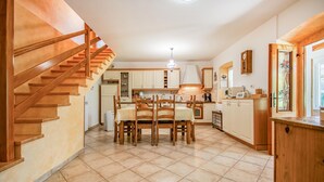 A kitchen with wooden cabinets, a dining table with chairs, a staircase, and a kitchen island. - 3 bedroom amazing home in Stanjel (Stanjel)