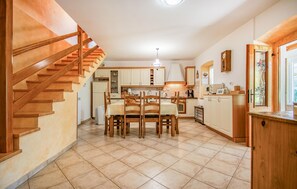 Une cuisine avec des meubles en bois, une table à manger avec des chaises, un escalier et un îlot de cuisine.