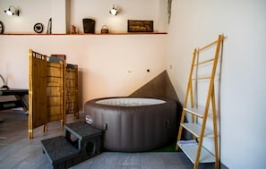 A room with a large round inflatable bed, a wooden ladder, a bamboo screen, and a shelf with various items.
