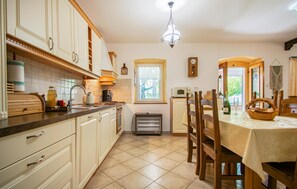 Une cuisine avec des meubles blancs, une cuisinière, un évier et un coin repas comprenant une table et des chaises.