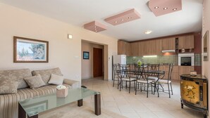 Een woonkamer met een glazen salontafel, een bank met kussens, een eethoek met een glazen tafel en stoelen, en een keuken met houten kastjes en een fornuis.
