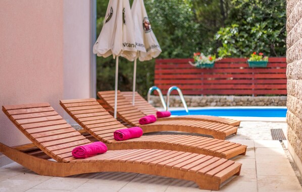 Un espace aménagé au bord de la piscine, avec des chaises longues en bois, une piscine et une clôture rouge.