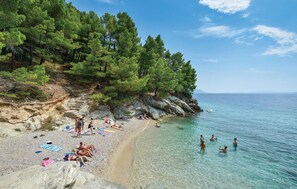 Une plage à l’eau claire, des gens qui prennent des bains de soleil et une falaise rocheuse bordée d’arbres.
