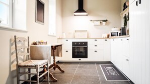 A modern kitchen with white cabinets, a black oven, and a dining area with a wooden chair and table. - Awesome home in Stavele with WiFi (Stavele)