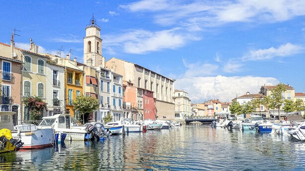 Un canal con barcos amarrados, edificios históricos y una torre.
