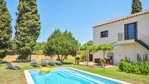 Una piscina con sillones de descanso, una pérgola y un edificio con balcón.