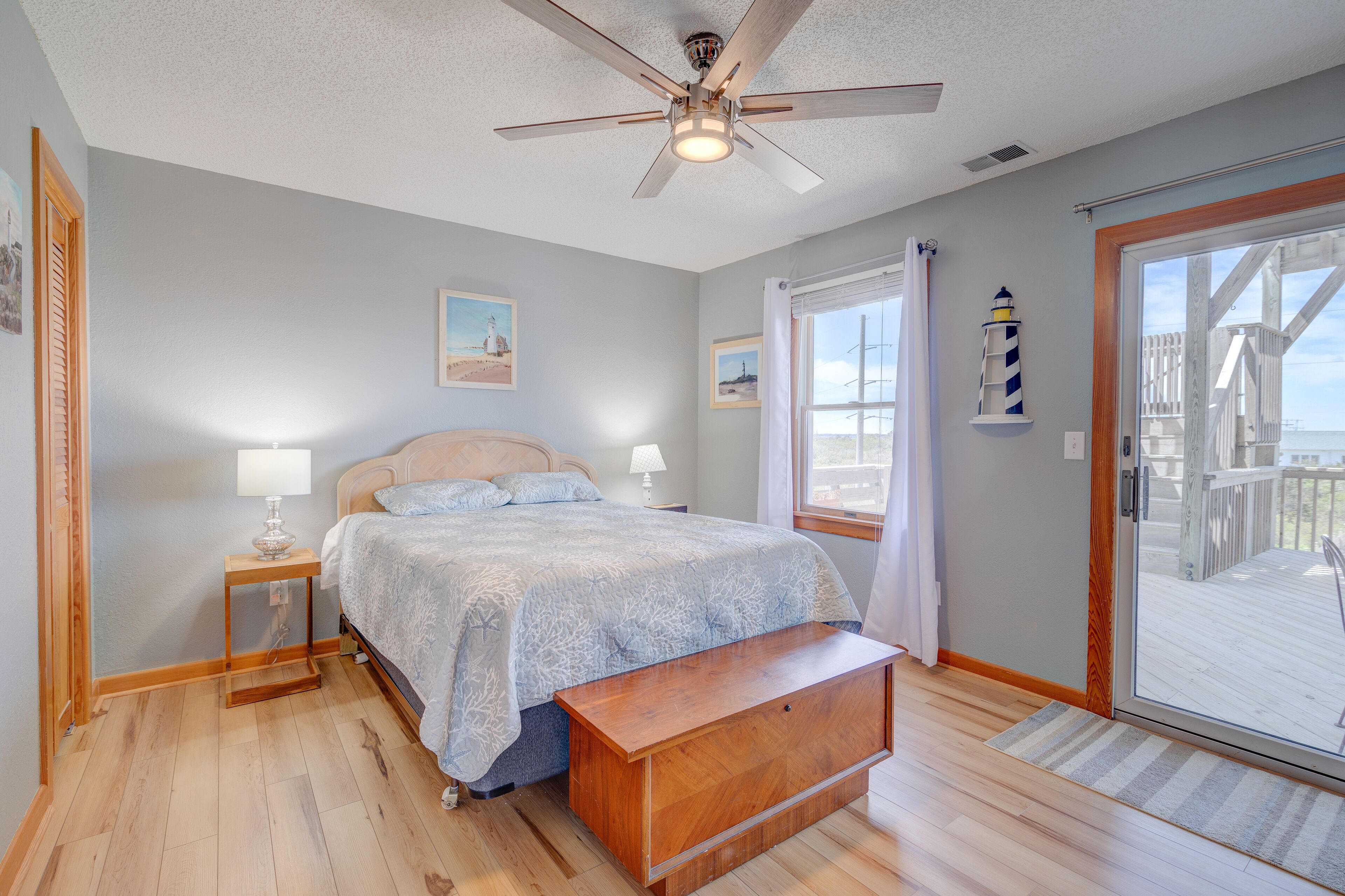 A bedroom with a bed, a nightstand, a wooden bench, a ceiling fan, and a view of the deck through a glass door.