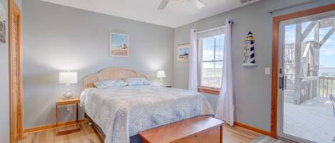 A bedroom with a bed, a nightstand, a wooden bench, a ceiling fan, and a view of the deck through a glass door.
