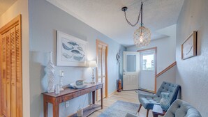 Un couloir avec une console en bois, un tapis à motifs bleus et un fauteuil à revêtement gris.