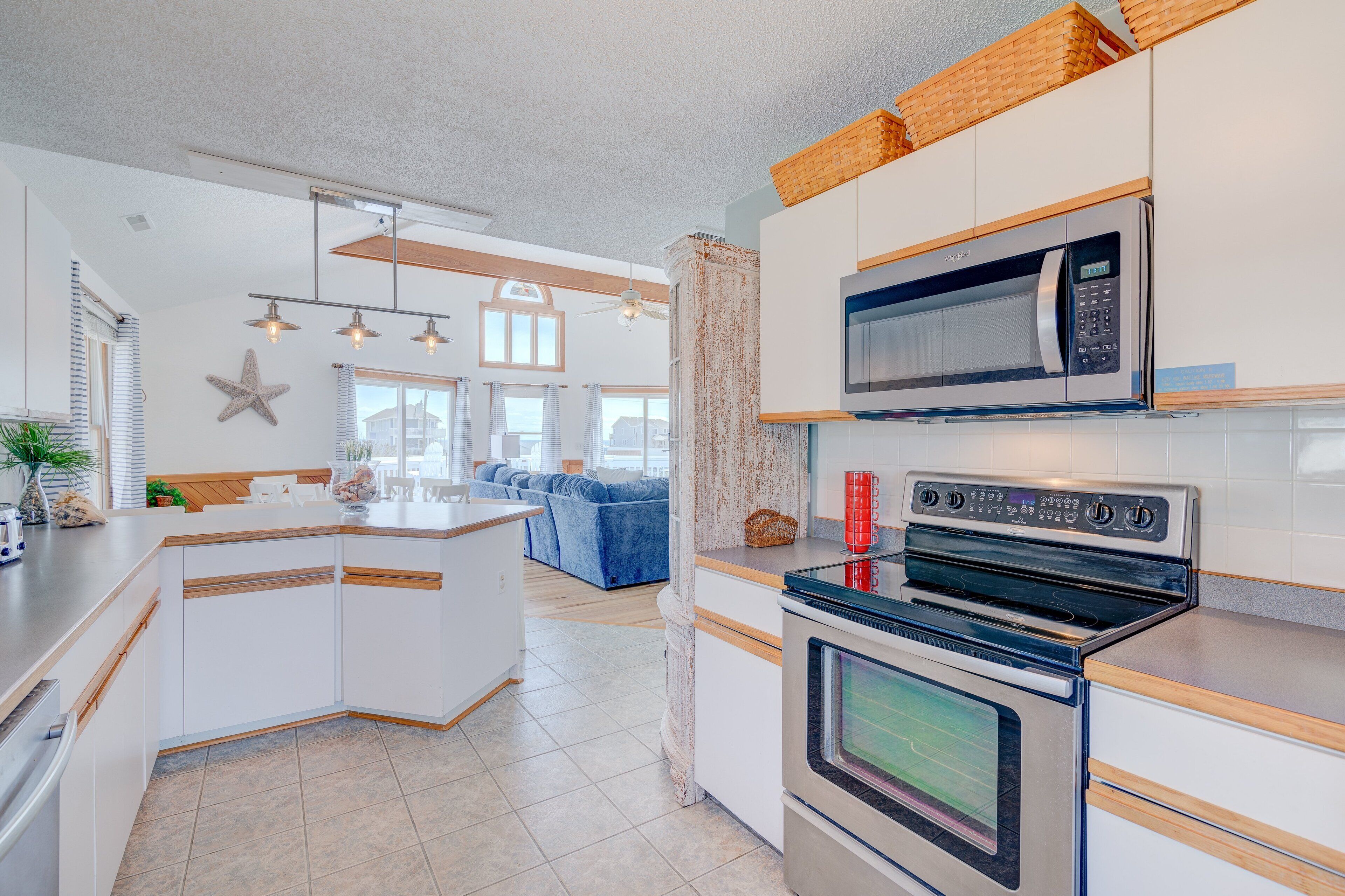 Une cuisine moderne avec des meubles blancs, un four encastré, un micro-ondes et un grand îlot central doté d’un évier.