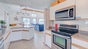Une cuisine moderne avec des meubles blancs, un four encastré, un micro-ondes et un grand îlot central doté d’un évier.