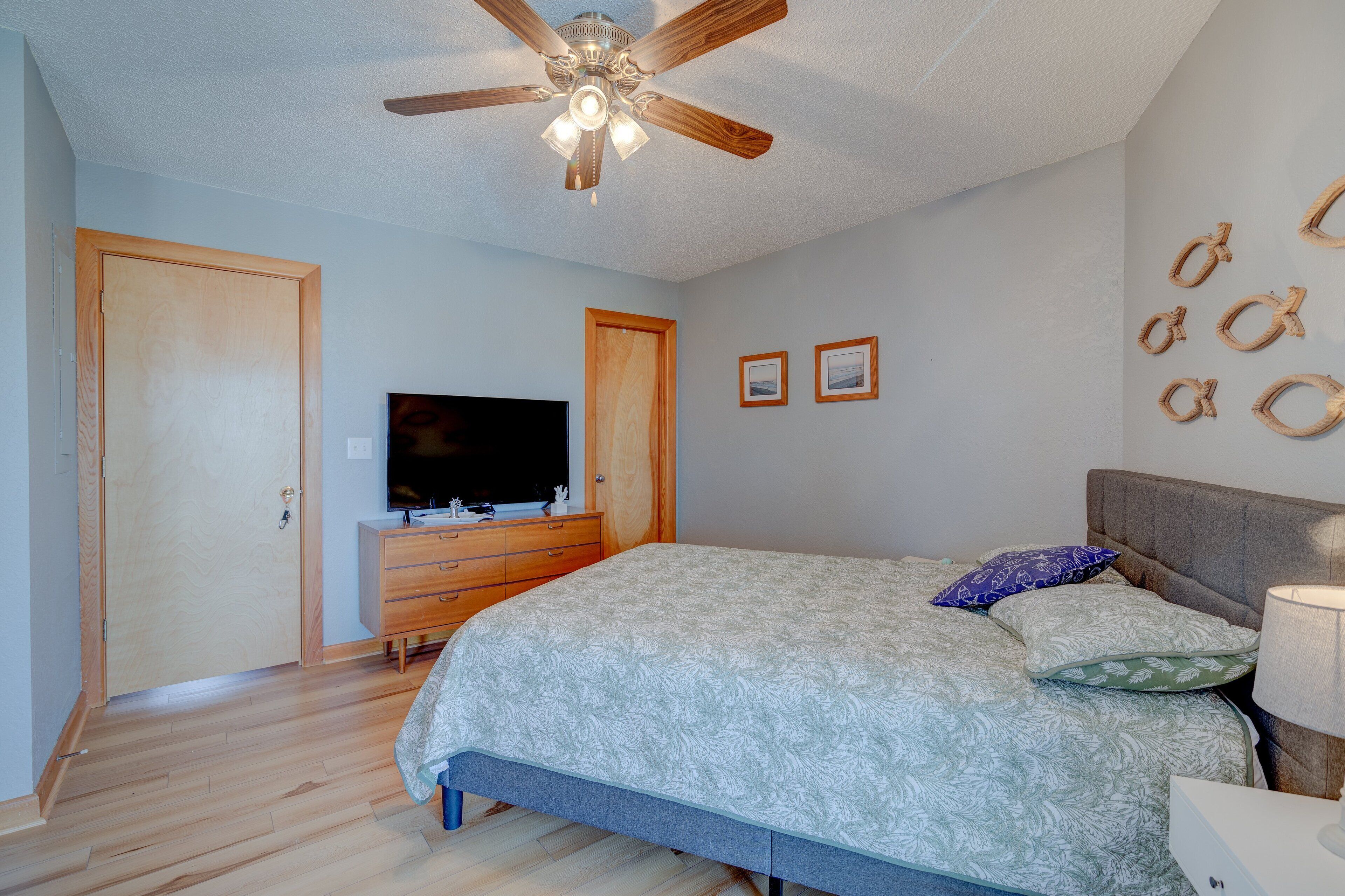 A bedroom with a bed, wooden wardrobe, television, ceiling fan, and wall decorations.