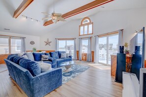 Ein großzügiges Wohnzimmer mit einer großen blauen Couch, Holzbalken, einem Deckenventilator und großen Fenstern mit Blick auf die Stadt.