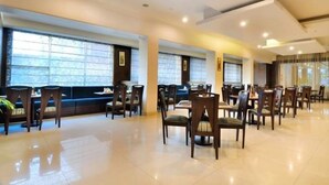 Un amplio comedor con varias mesas y sillas, ventanas grandes con persianas y un diseño moderno y limpio.